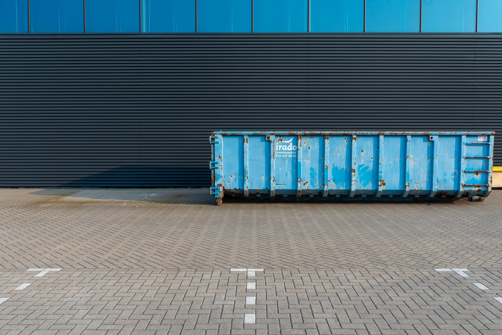 A blue roll-off container against a dark warehouse wall