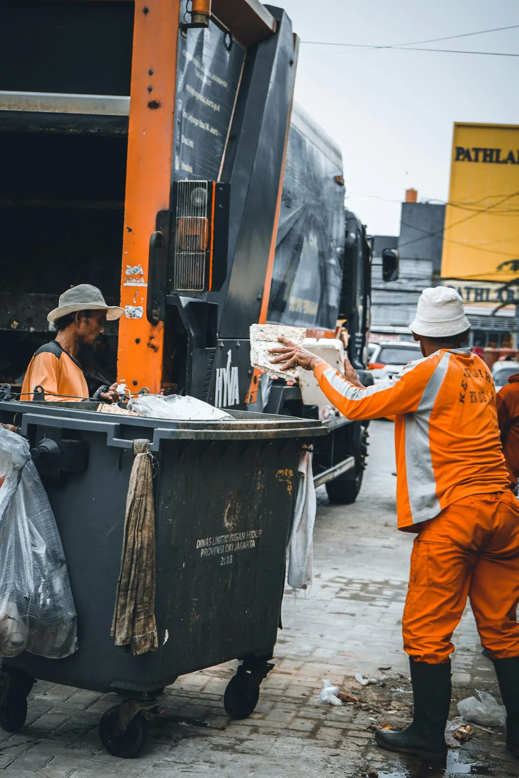 A crew loading a container into an orange refuse truck