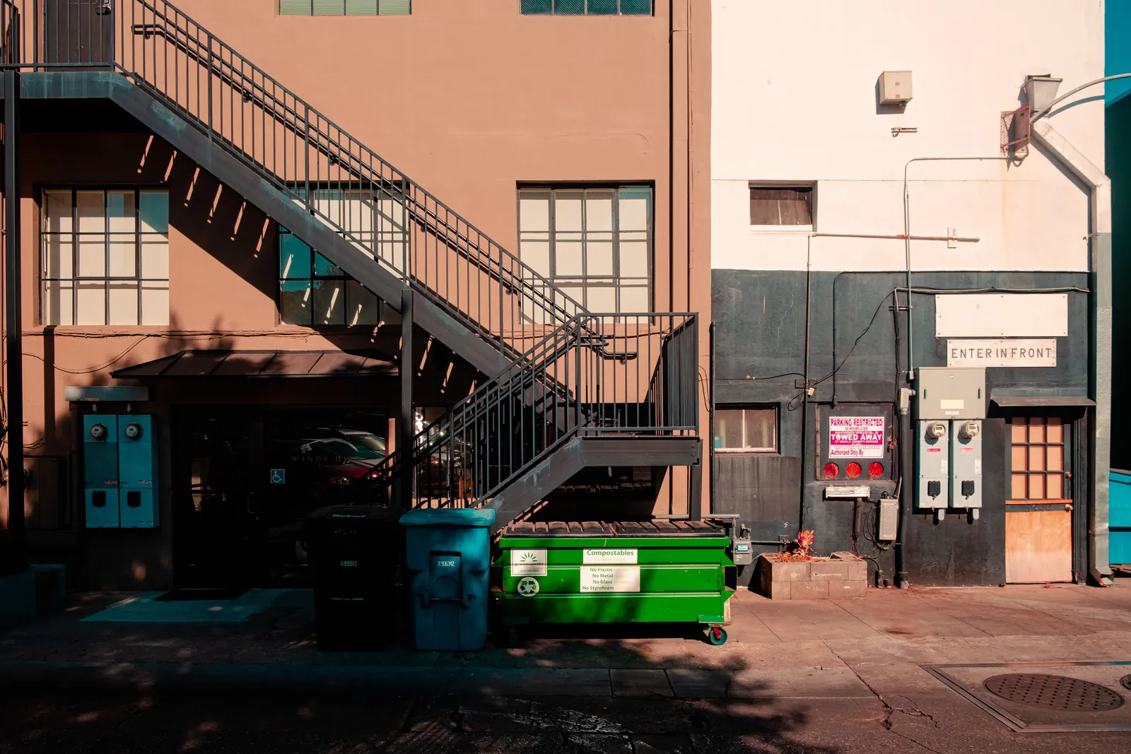 A green compostables dumpster under a fire escape