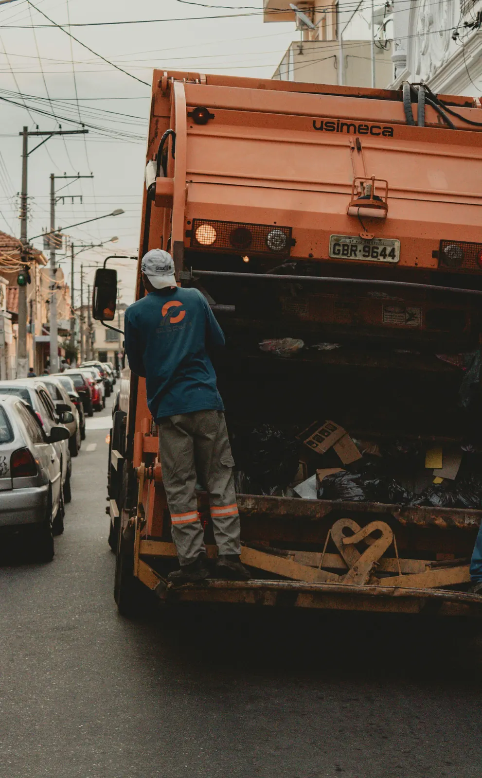A loader riding the rear step of a refuse truck