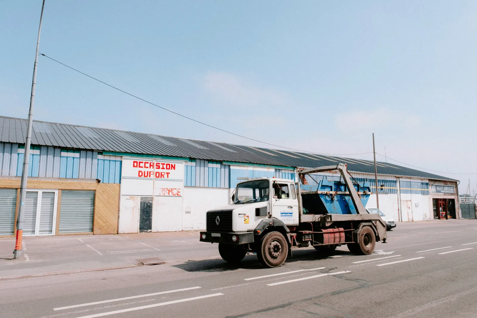 A skip loader carrying a blue skip on its lifting arm